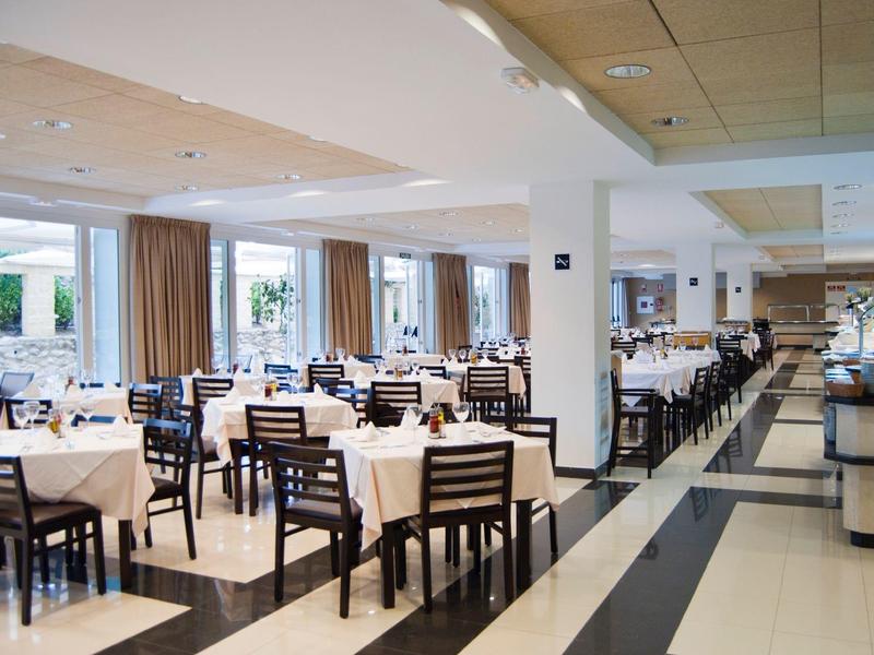 Ampia sala da pranzo con molti tavoli apparecchiati e sedie in tonalità neutre.