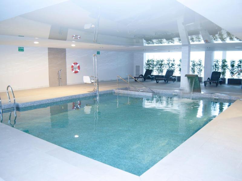 Piscina interna con sdraio e grandi finestre in un hotel.