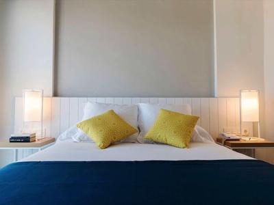 Chambre d'hôtel simple avec lit double, deux coussins jaunes et tables de chevet avec lampes.