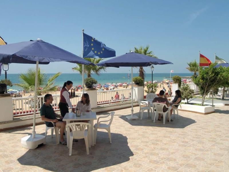Terrasse avec des tables et des parasols bleus surplombant la mer par une journée ensoleillée.