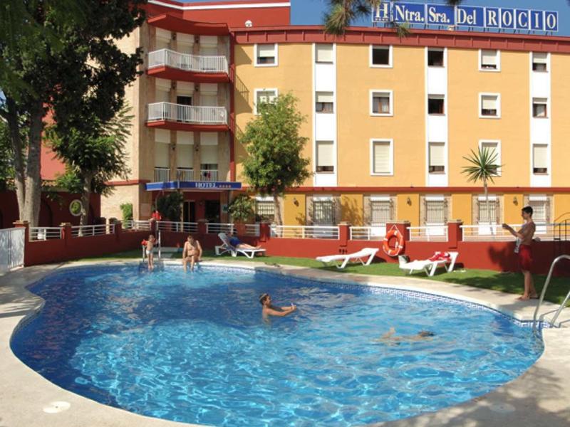Piscine d'hôtel ronde avec eau bleue, entourée de pelouse et terrasse ensoleillée.