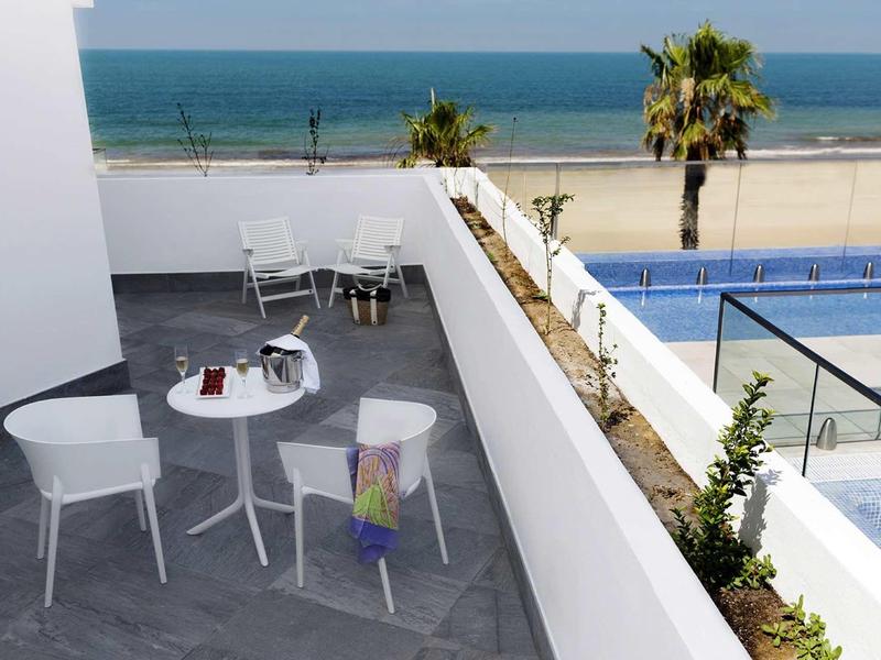 Balcon moderne avec tables et chaises, piscine et vue sur la mer en arrière-plan.