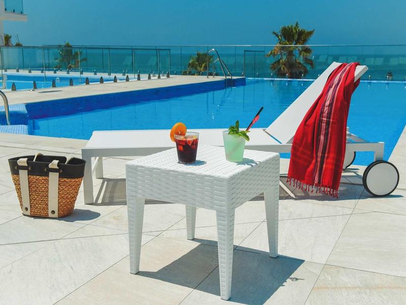 Terrasse avec table blanche, deux boissons, sac en osier et piscine avec vue sur la mer.