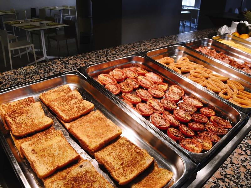 Buffet avec pain grillé, tomates grillées et saucisses dans une salle à manger.