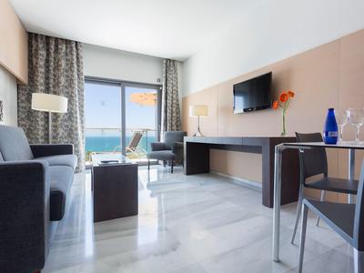 Habitación de hotel moderna con vista al mar, sofá, escritorio y ventana grande.