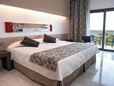 Habitación de hotel moderna con cama doble, mesillas, ventana grande y balcón con vistas al mar.