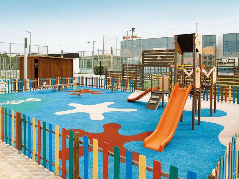 Colorful outdoor playground with slides, fenced, located in front of modern buildings.