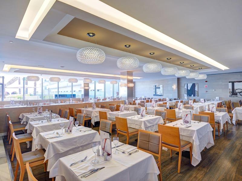 Bright, modern hotel restaurant with white tablecloths and wooden furniture.