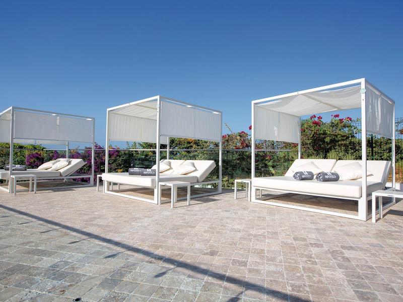 Three modern white outdoor lounges with cushions on stone flooring under a blue sky.