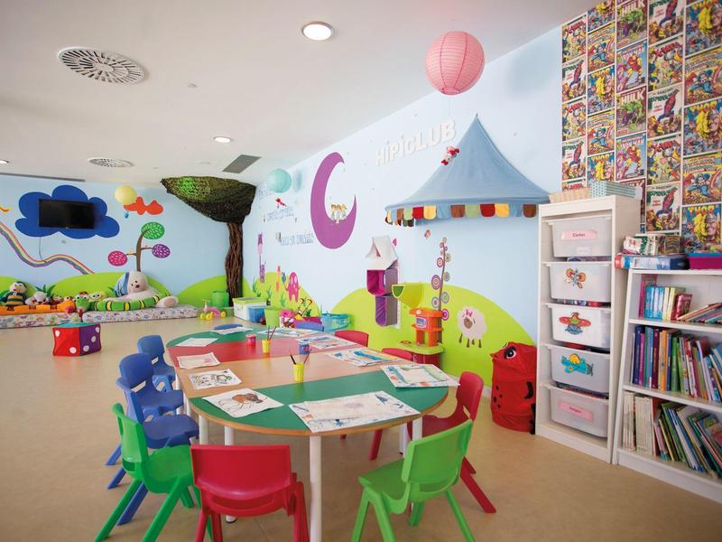 Colorful children's playroom with tables, chairs, bookshelf, and wall decorations.