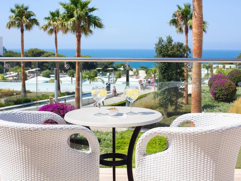Two white garden chairs around a small round table overlooking palm trees and the sea.