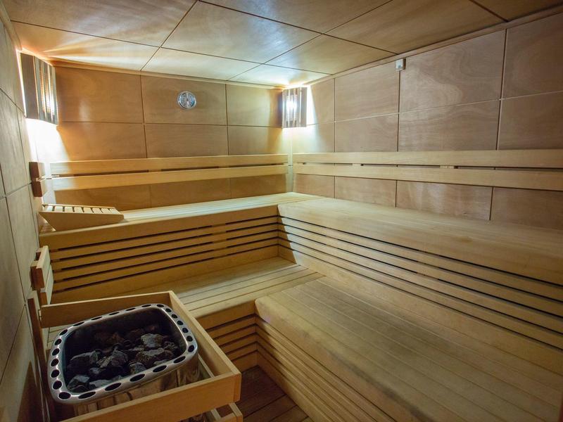 Bright sauna cabin with wooden benches and a sauna heater in the corner.
