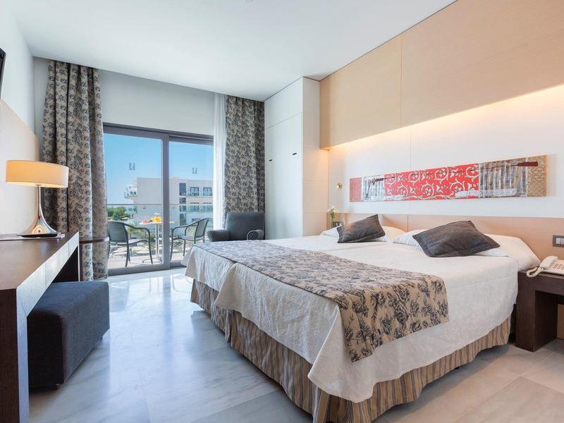 Modern hotel room with double bed, large window, and balcony with seating area.