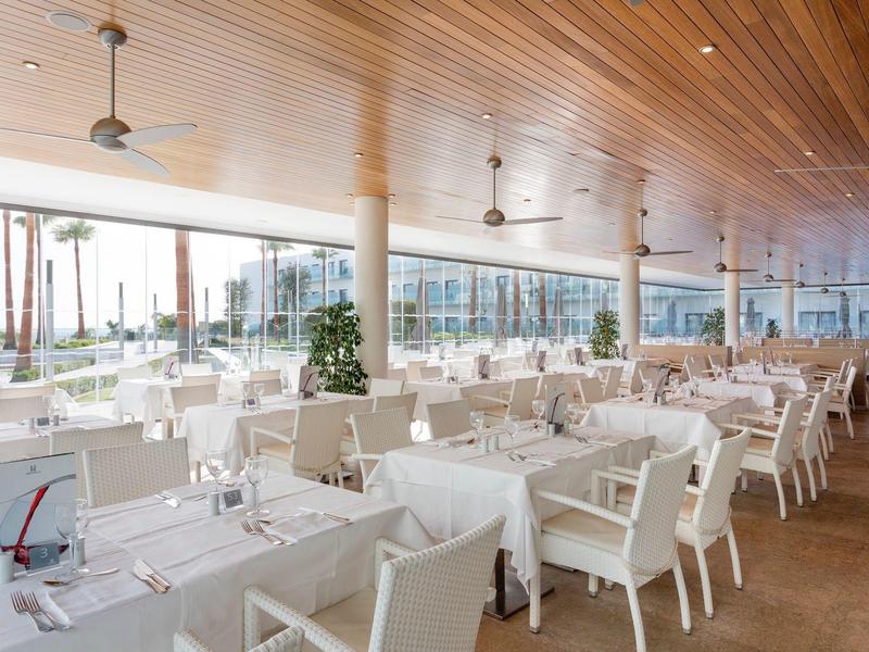 Bright restaurant with wooden ceiling, white tables and chairs, and large windows.
