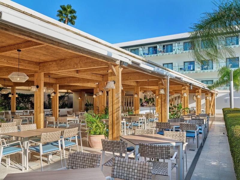 Hotel outdoor area with covered seating and modern furniture under a blue sky.