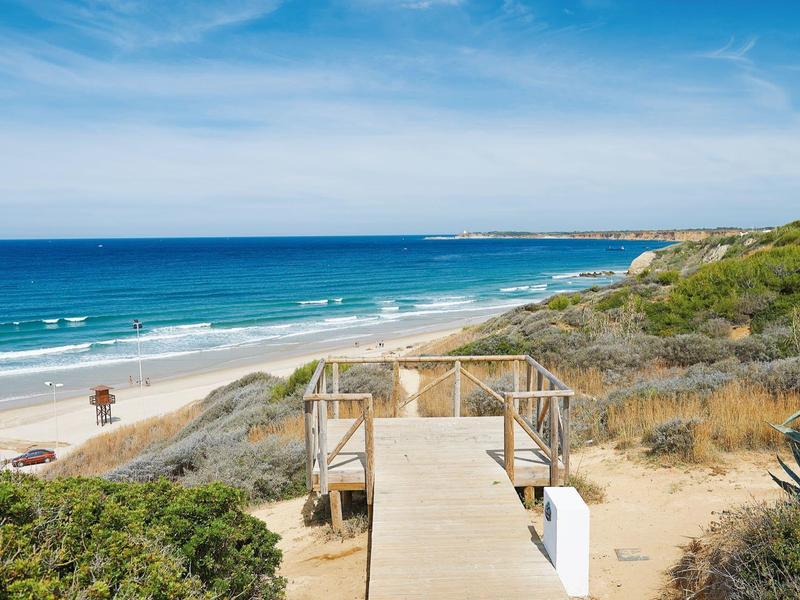 Wooden pathway leads to a white sandy beach with blue sea and vegetated dunes