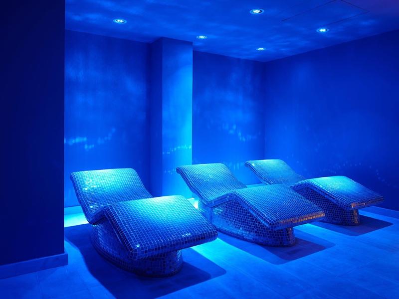 Dim relaxation room with three illuminated loungers and blue lighting.