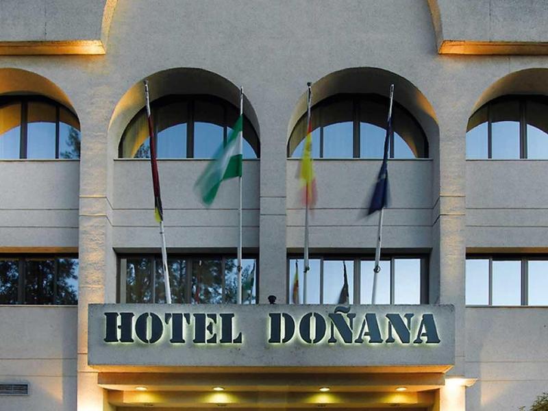 Fassade des Hotels Donana mit geschwungenem Dach und beleuchtetem Eingangsbereich bei Dämmerung.