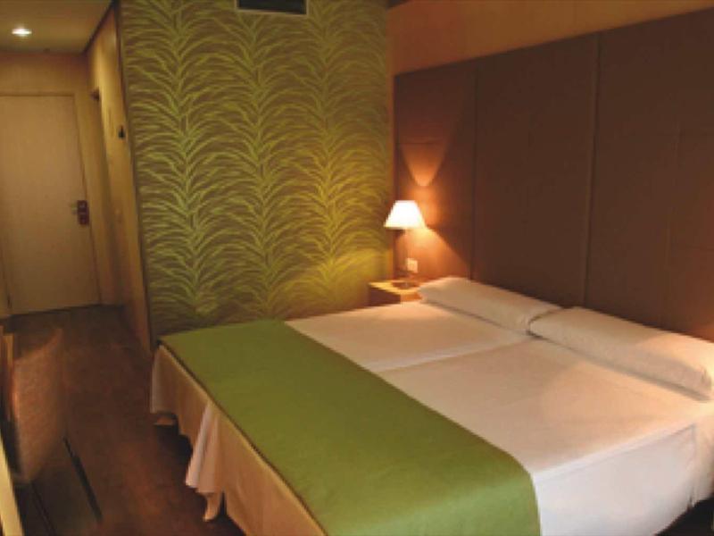 Kleines Schlafzimmer mit zwei Einzelbetten, grüner Tagesdecke, Holzmöbeln und warmem Licht.