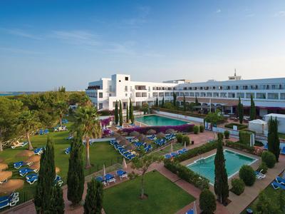 Duży hotel z basenem, leżakami i zadbanym ogrodem pod czystym niebem.