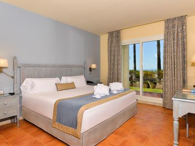 Heldere hotelkamer met groot bed, nachtkastjes en uitzicht op de tuin door het raam.