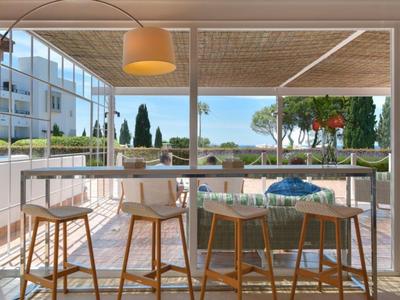 Lichte hotelterras met stoelen, tafels en uitzicht op zee bij zonnig weer.