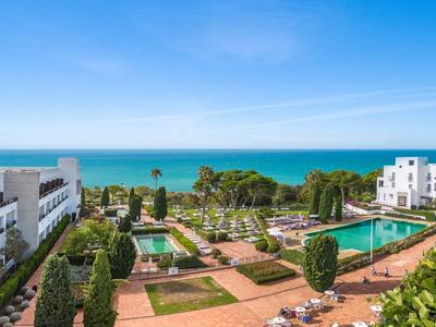Uitzicht op een hotelresort met zwembaden, tuinen en een blauwe zee onder een heldere hemel.