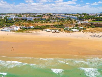 Breid zandstrand met zachte golven en hotels en groen erachter.