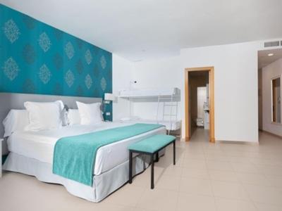 Helles Hotelzimmer mit großem Bett, türkisfarbenem Akzent und einfachem, modernem Design.