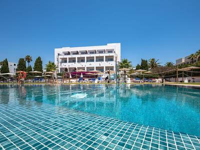 Moderne hotelzwembad met helder blauw water en parasols onder een blauwe lucht.