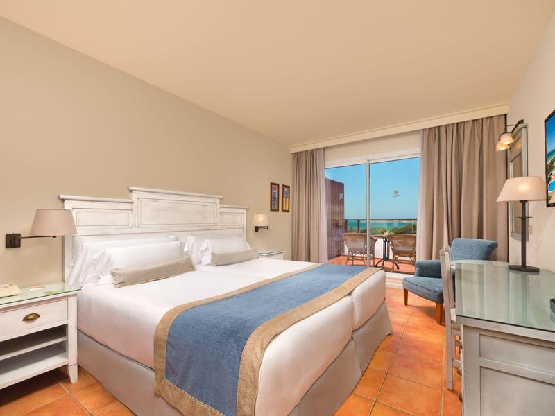 Lichte hotelkamer met tweepersoonsbed, balkon en zeezicht bij daglicht.