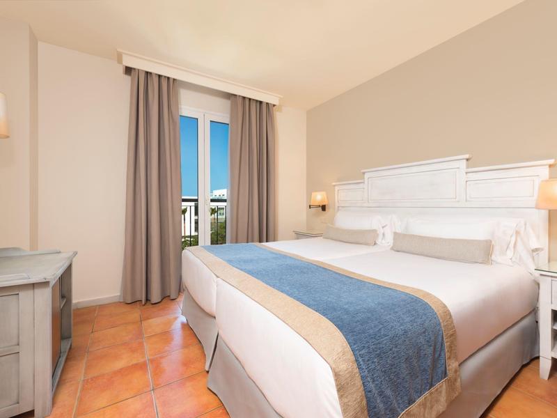 Helder ingericht hotelkamer met groot bed, blauw-beige dekbed en uitzicht op balkon.