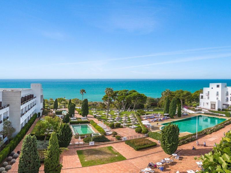 Uitzicht op een hotelresort met zwembaden, tuinen en een blauwe zee onder een heldere hemel.