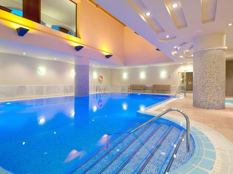 Overdekt zwembad met blauwe tegels, metalen leuning en warme indirecte verlichting.