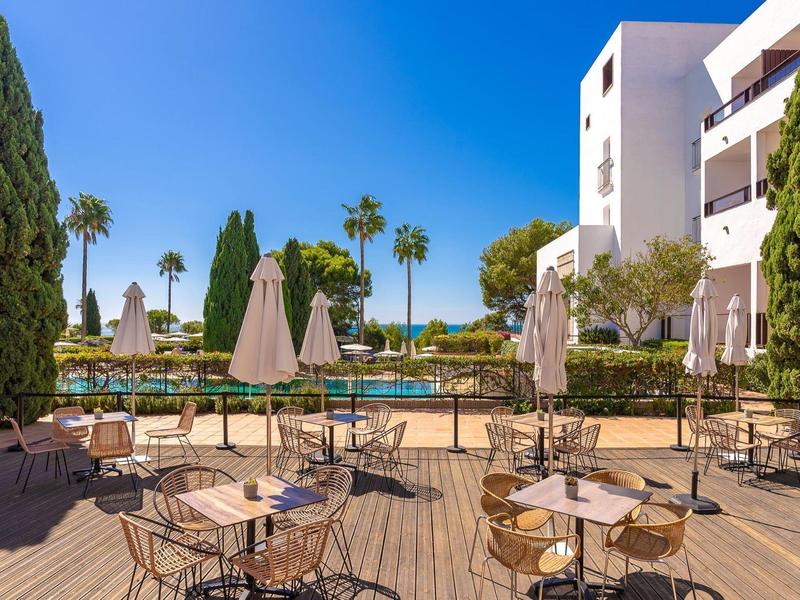 Terras met tafels en stoelen voor hotelgebouw onder een heldere hemel