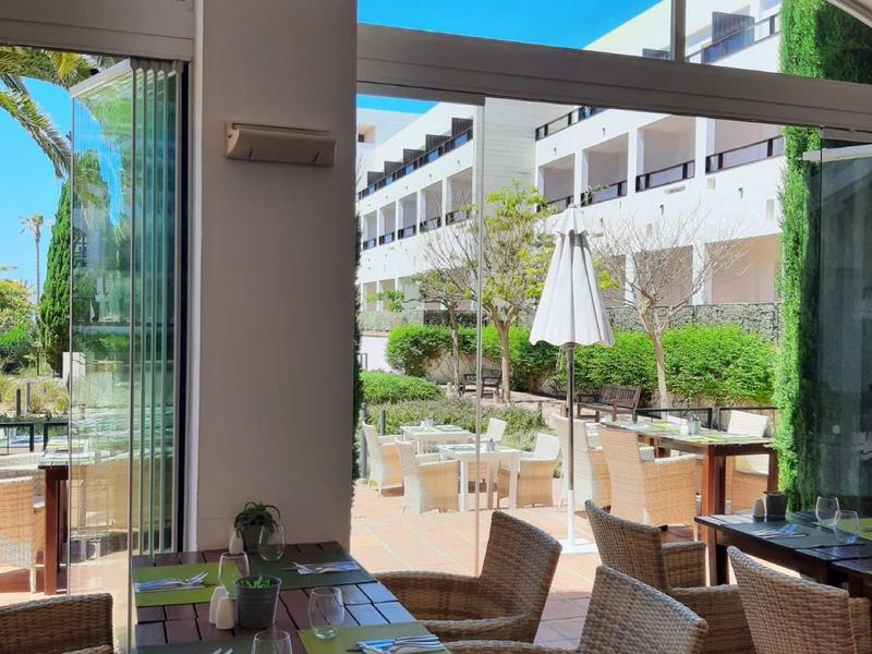 Moderne binnenruimte met rieten stoelen en uitzicht op een zonnig buitenterras van een hotel.