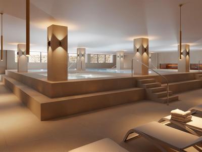 Piscina interna moderna in un elegante hotel benessere con illuminazione calda e sdraio.