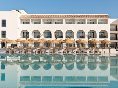 Nowoczesny kompleks hotelowy z dużym basenem i parasolami przed jasnymi budynkami.