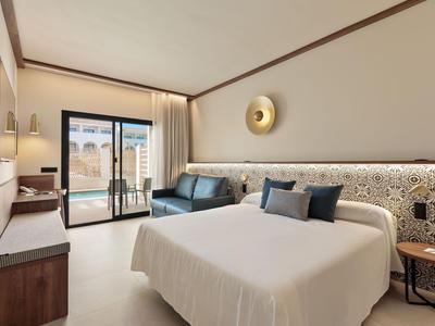 Nowoczesny pokój hotelowy z dużym łóżkiem, skórzaną sofą, balkonem i jasnym oświetleniem.