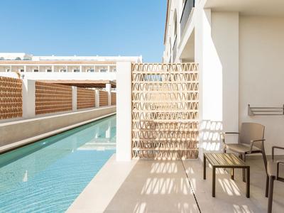 Nowoczesny balkon hotelowy z widokiem na basen, jasnym murem i wygodnym miejscem do siedzenia.