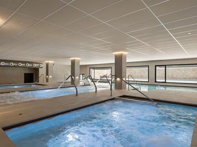 Nowoczesna strefa basenu wewnętrznego z jacuzzi i dużymi oknami z widokiem na zewnątrz.