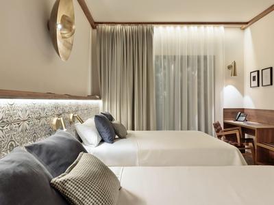 Nowoczesny pokój hotelowy z dwoma łóżkami, jasnymi zasłonami i drewnianymi meblami.