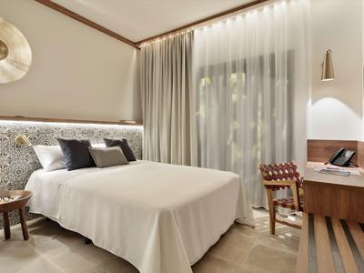 Nowoczesny pokój hotelowy z łóżkiem podwójnym, drewnianymi detalami i oknem z przezroczystymi zasłonami.
