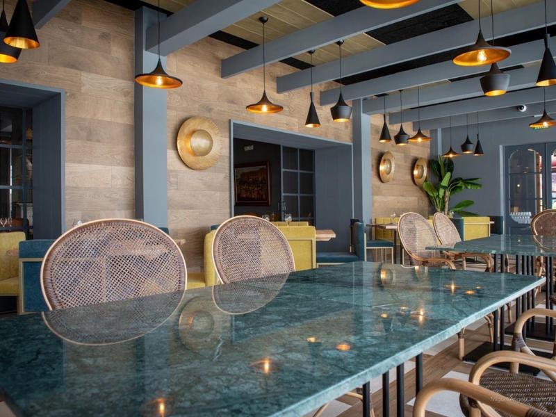 Moderne eetruimte met glazen tafel, rieten stoelen, stenen muren en zwarte hanglampen.