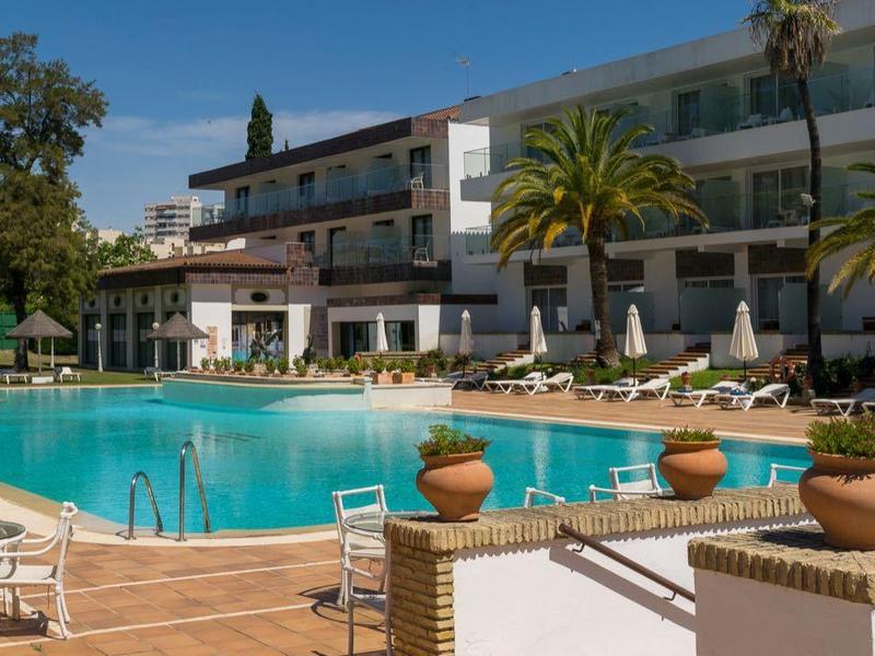Buitenzwembad van hotel met ligstoelen, palmbomen en zonnig weer.