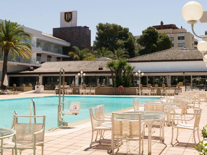 Buitenzwembad met witte tafels en stoelen bij een hotel en palmbomen.