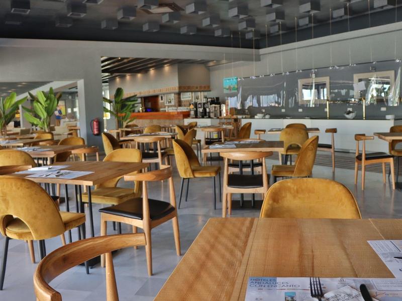 Ruime hotel eetzaal met houten tafels en mosterdgele stoelen, modern ontwerp.