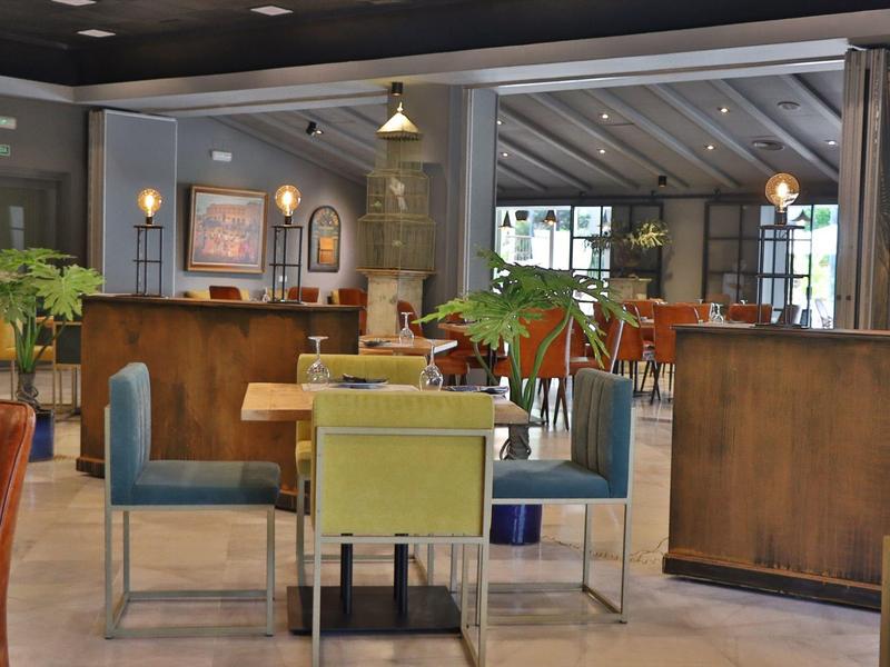 Moderne eetruimte in hotel met kleurrijke stoelen en planten op lichte tegelvloer.