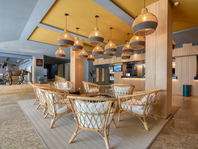 Moderne hotellobby met houten meubels, hanglampen en open zithoek.