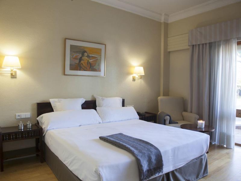 Gezellige hotelkamer met twee eenpersoonsbedden, nachtkastjes, fauteuil en balkondeur met gordijnen.